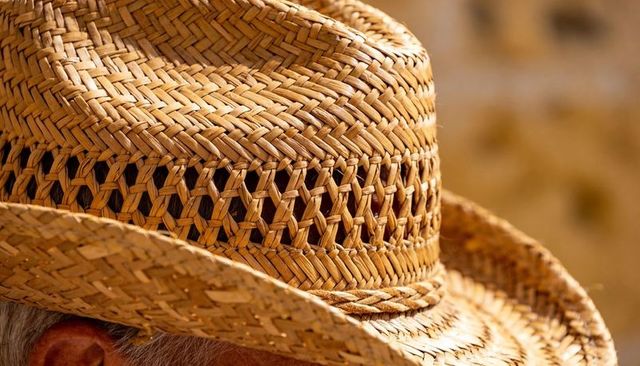 Wearing sunlit woven straw hat with braided crown and visible gray hair close-up
