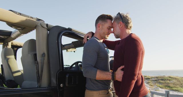 Happy caucasian gay male couple standing by car embracing on sunny day at the beach. summer road trip and holiday in nature.