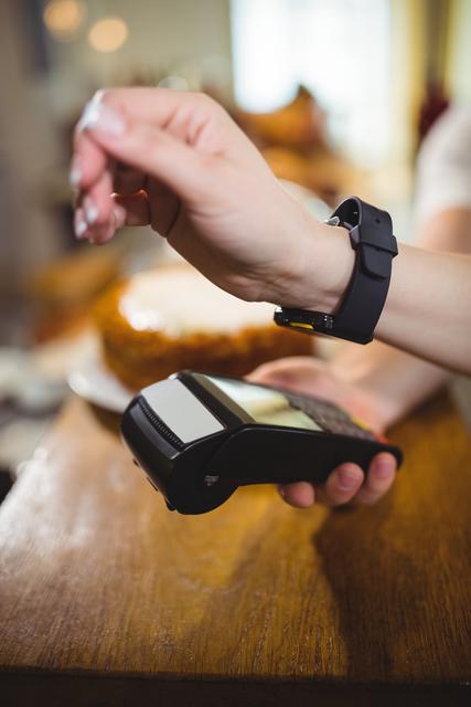 Mid-section view of a woman paying bill through smartwatch using NFC technology in cafe. Emphasizes modern, convenient, and cashless payment methods. Useful for illustrating digital payments, wearable technology's role in everyday transactions, and the convenience of contactless payments in retail settings.