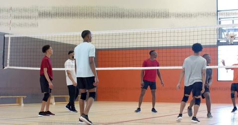 Teen athletes practicing indoor volleyball, executing block at net during team training