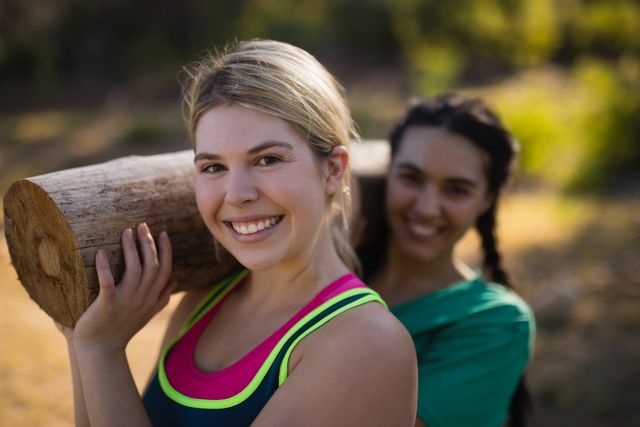 Portrait of trainer and woman carrying heavy wooden log during obstacle course