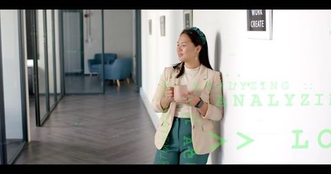 Asian professional leaning in modern hallway holding pink mug with data overlay