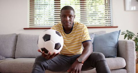 Young Man Enthusiastically Holding Soccer Ball on Gray Sofa