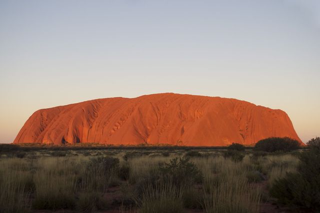 This image showcases Uluru, a large sandstone monolith in the Australian Outback, bathed in the warm hues of sunset. This natural wonder is a significant landmark and a popular tourist destination. Ideal for use in travel brochures, educational materials about natural landmarks, tourism promotions, and articles on Australian geography and culture.