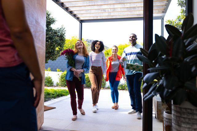 Group of diverse friends arriving at a house with gifts and flowers, smiling and happy. Ideal for use in content related to celebrations, social gatherings, friendship, hospitality, and welcoming guests.