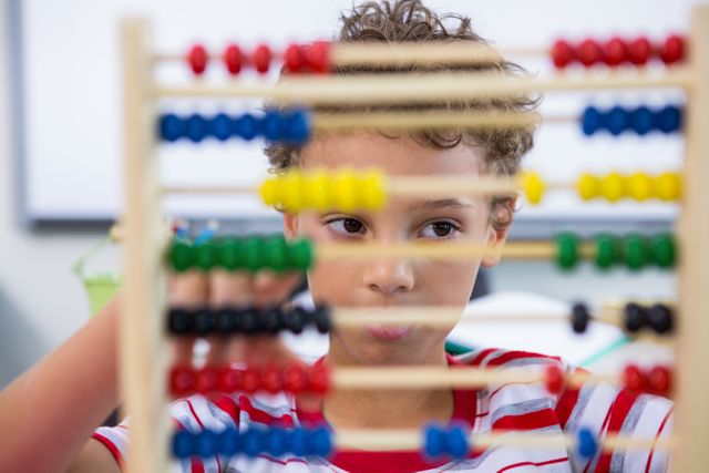 Close-up of boy playing with abacus in classroom