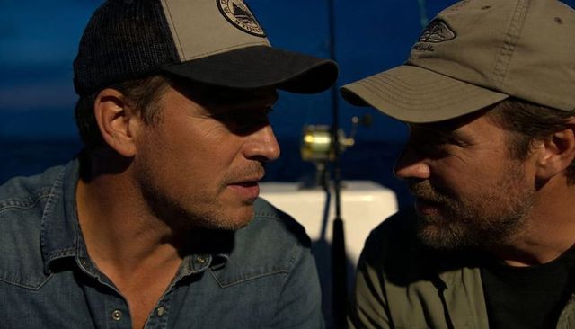 Two men conversing on fishing boat at dusk, close-up portrait with fishing rod