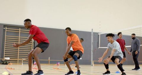 Diverse male volleyball players practicing low passing drill in indoor gym team training