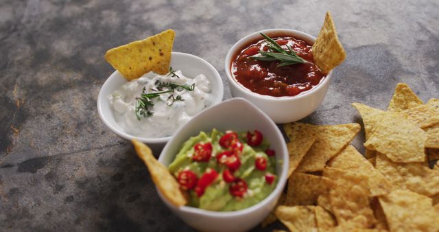 Tasty nachos paired with guacamole, salsa, and sour cream dips arranged on a rustic table. Ideal for illustrating Mexican cuisine, party appetizers, or snack ideas for gatherings. Useful for culinary blogs, restaurant menus, social media posts, or food-related advertisements.
