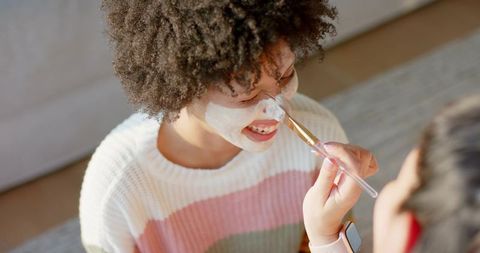 Parent applying facial mask to african american child smiling during tender at-home skincare
