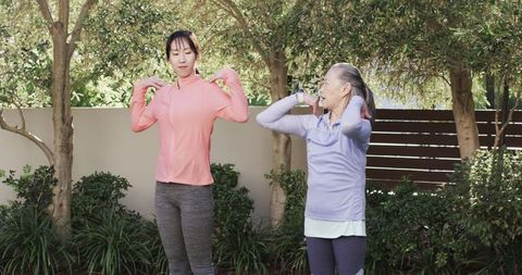 Mother and daughter stretching in garden wearing fitness trackers
