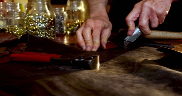 Artisan shaping a piece of leather using hand tools at a workbench. Hands prominently visible, indicating precision and skill in traditional leathercraft. Ideal for use in articles or advertisements related to handmade products, traditional crafts, artisan workshops, DIY projects, and hobby activities.