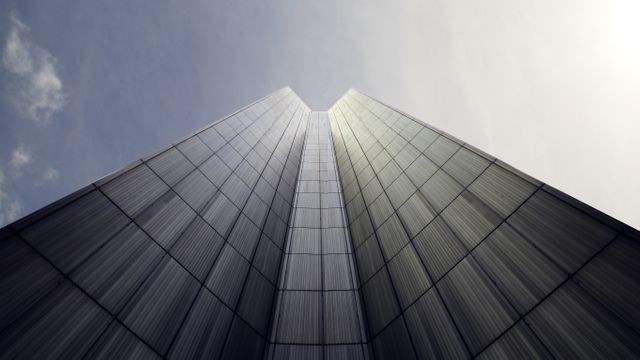 Modern skyscraper with reflective glass facade reaching into sky, exemplifies urban architecture. Suitable for marketing materials, architectural designs, urban development projects, or website banners about modern cityscapes.