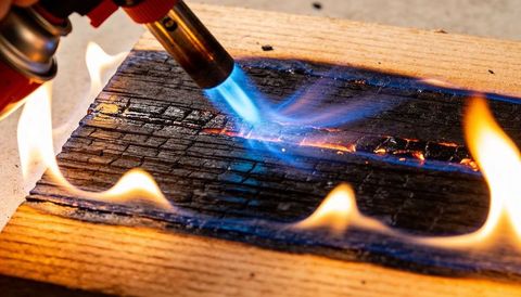 Blowtorch charring wood plank creating deep charred texture for shou sugi ban finish