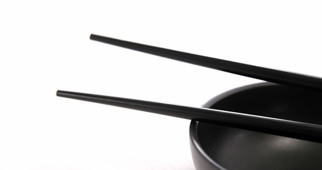 A pair of black chopsticks rests on a matching bowl, with copy space. Chopsticks are commonly used in Asian cuisine for picking up food.