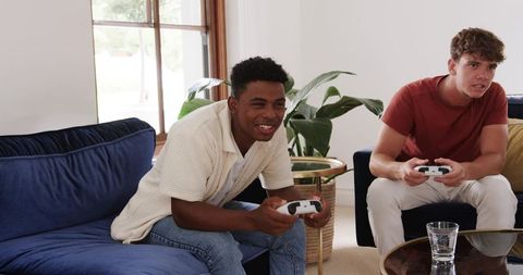 Young Black and White friends playing video games on couch, competitive home gaming
