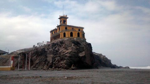 Historic Yellow Building on Rocky Beach Cliff on Cloudy Day