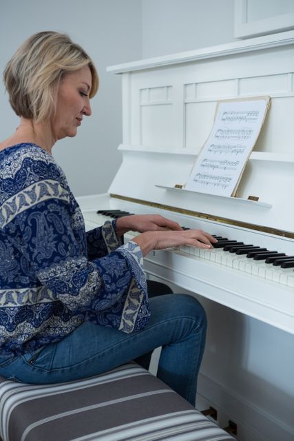Woman playing piano in a home setting, wearing casual clothing. Ideal for use in articles or advertisements related to music, hobbies, home life, relaxation, and lifestyle.