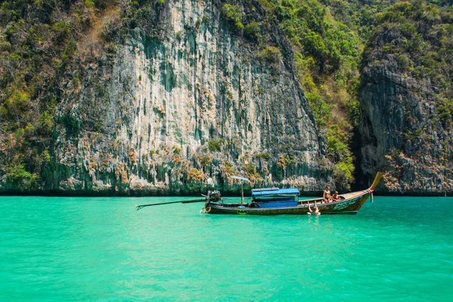 Traditional Thai longtail boat floating on crystal clear turquoise water near towering cliffs in Krabi, Thailand. Ideal for tourism, travel blogs, adventure promotions, and vacation advertising.