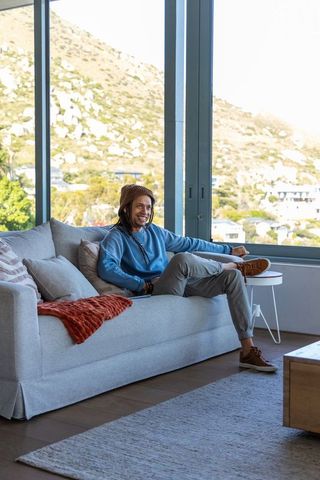 African american man relaxing on light-gray sofa beside floor-to-ceiling window with mountain view