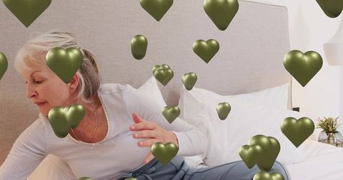 Senior woman reaching across bed with green heart overlays in cozy bedroom