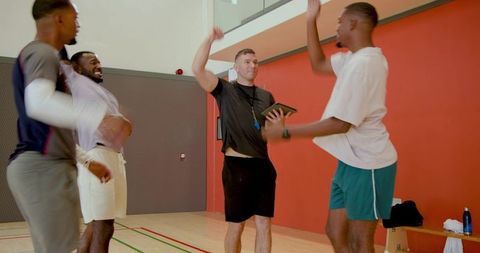 Coach celebrating team win on indoor court with clipboard, whistle and high-fives