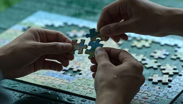 Hands connecting jigsaw pieces on wet tabletop, showing teamwork and concentration