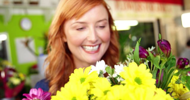 Woman smiling happily while holding bright fresh flowers in a flower shop. Ideal for themes related to happiness, flower arrangements, springtime, floral gifts, flower shops, or positive emotions.