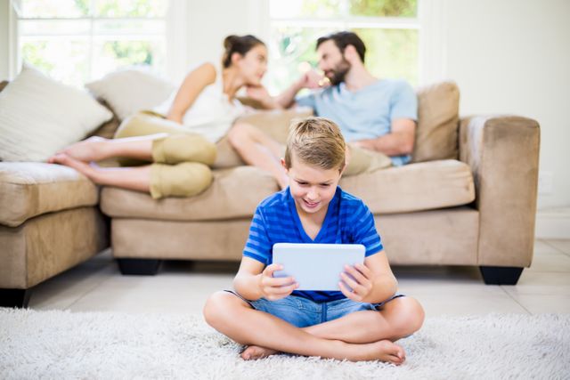 Boy using a digital tablet while parents sitting on sofa in background at home