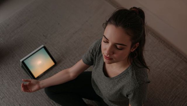 Young woman meditating indoors with glowing tablet for guided mindfulness practice