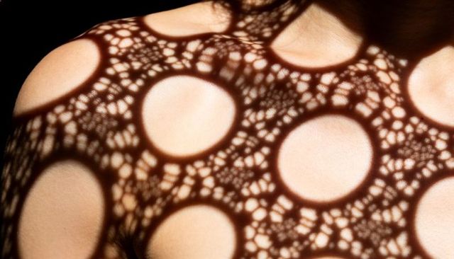 Lacy circular shadow casting across woman chest and shoulder with high-contrast pattern