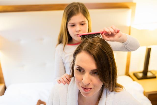 Daughter combing her mothers hair in bedroom at home