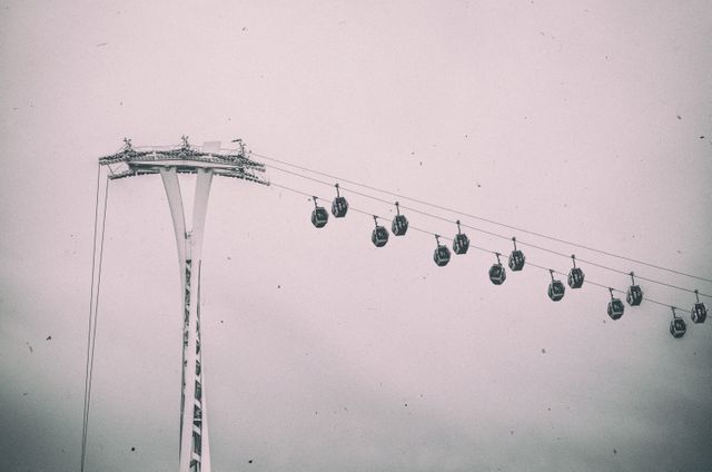 Depicts vintage aerial cable cars suspended high on wires in a cloudy sky. The sepia tone adds a nostalgic and eerie effect which makes this image ideal for use in travel blogs, retro-themed designs, transportation articles, or creative projects highlighting nostalgia and amusement parks.