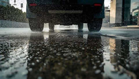 Car tires splashing water on wet urban street with undercarriage reflections