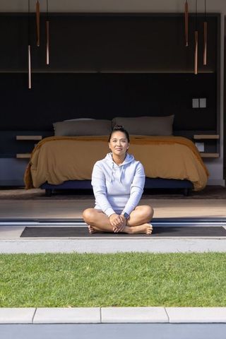 Asian woman sitting at bedroom threshold in hoodie practicing morning meditation with smartwatch