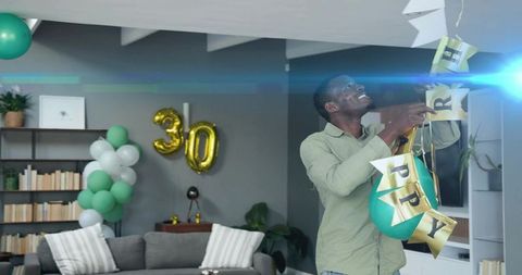 Smiling man hanging gold happy banner with teal balloons for 30th birthday in living room