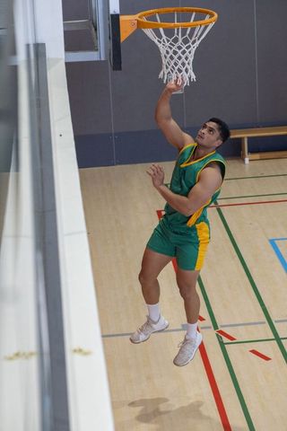 Athlete dunking in indoor basketball court wearing green and yellow uniform