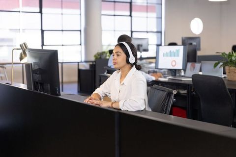 Focused woman wearing headphones typing on computer in modern office