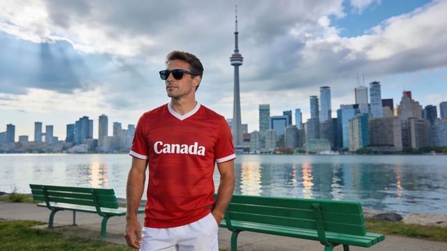 Confident man wearing canada jersey standing on toronto waterfront with cn tower skyline