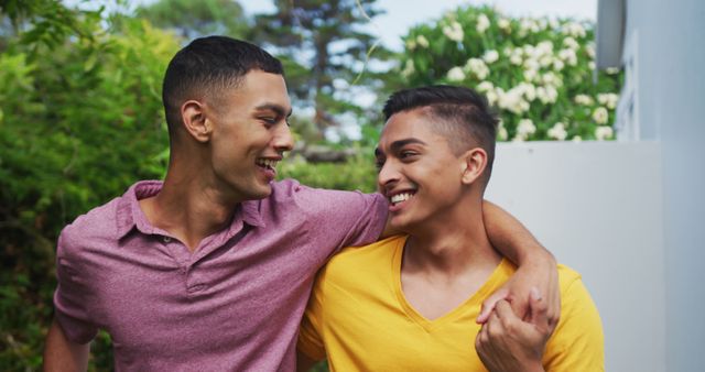 Smiling biracial gay male couple walking in garden hugging and kissing. staying at home in isolation during quarantine lockdown.