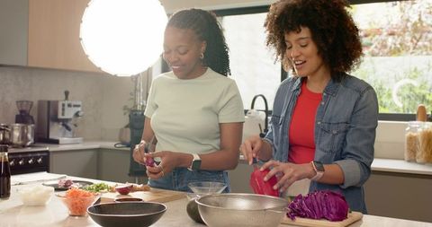 Diverse friends prepping colorful vegetables at kitchen island under studio light, smiling