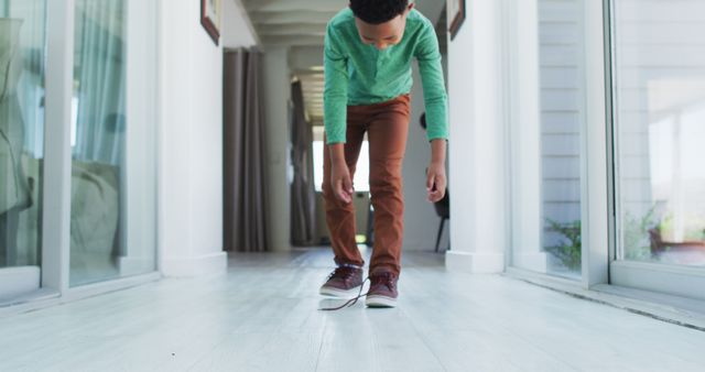 African american boy standing in hallway tying his shoes. staying at home in self isolation during quarantine lockdown.