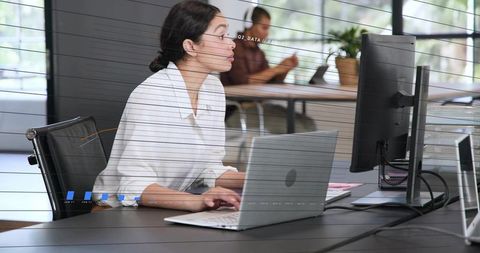 Focused professional typing while glancing at external monitor in modern coworking office