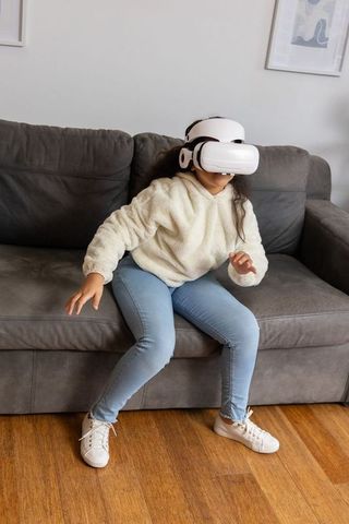Young girl experiencing virtual reality on couch wearing cream sherpa hoodie at home