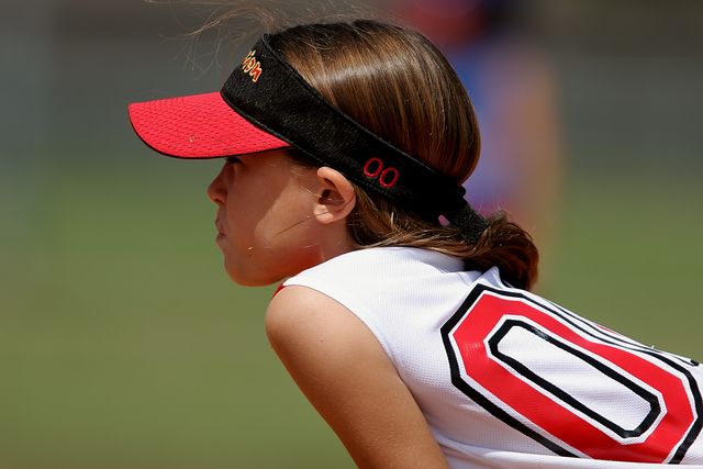 Young girl in baseball uniform and cap concentrating on game. Great for use in sports articles, children's sports, youth athletics promotions, team spirit content, and motivational materials.