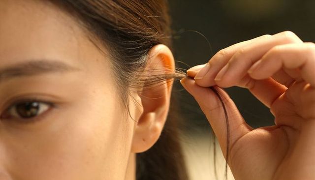 Tucking hair behind ear closeup featuring natural skin texture, brown strand and gentle hands