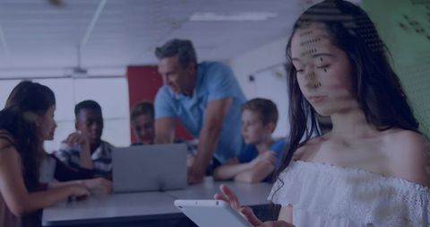 Teen girl using tablet while classmates collaborating with teacher in modern classroom