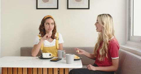 Two women chatting over coffee and pastries in sunlit modern dining nook