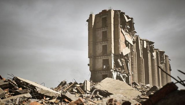 Crumbling concrete building standing among rubble with exposed floors and twisted rebar