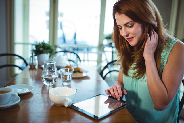 Woman using digital tablet with cup of coffee on table in cafe